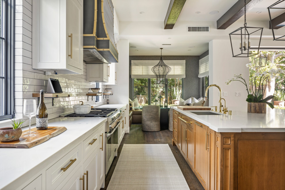 Large tuscan l-shaped dark wood floor, brown floor and exposed beam eat-in kitchen photo in Los Angeles with an integrated sink, shaker cabinets, white cabinets, marble countertops, white backsplash, subway tile backsplash, stainless steel appliances, an island and white countertops