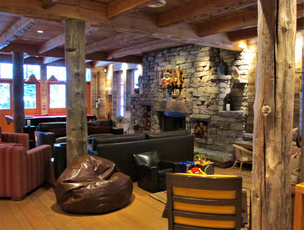 Example of a large mountain style light wood floor home office design with a wood stove and a stone fireplace