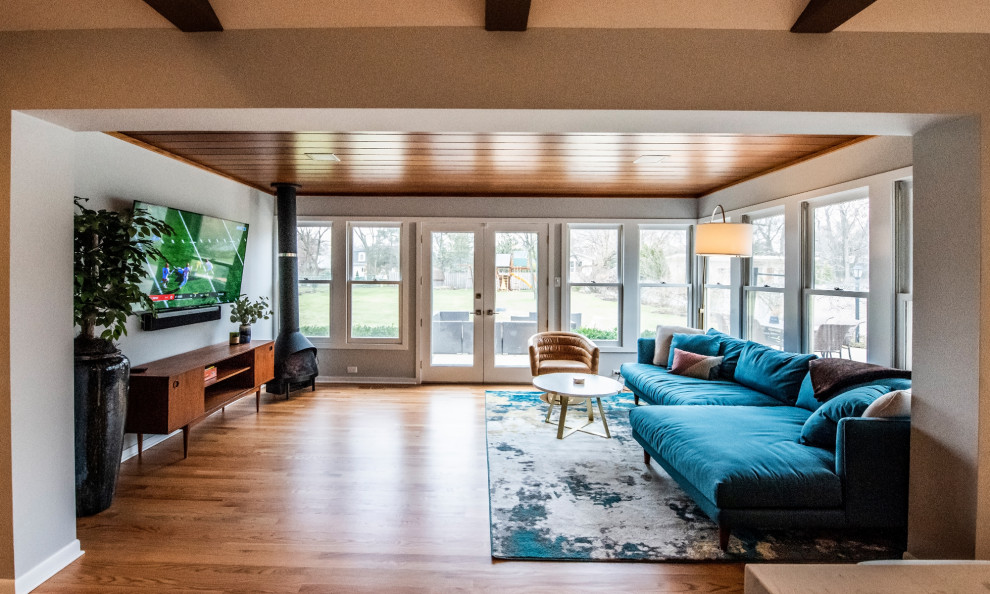 This is an example of a large midcentury open concept family room in Chicago with medium hardwood floors, brown floor, grey walls, a wood stove and a wall-mounted tv.