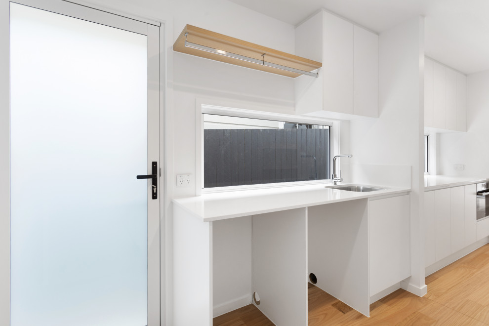 Inspiration for a single-wall dedicated laundry room in Brisbane with a drop-in sink, flat-panel cabinets, white cabinets, window splashback, a side-by-side washer and dryer, brown floor and white benchtop.