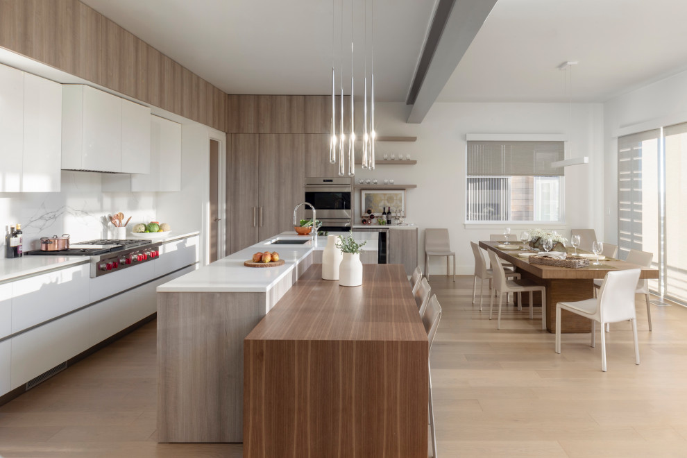 Example of a large trendy light wood floor and beige floor eat-in kitchen design in Salt Lake City with flat-panel cabinets, white cabinets, white backsplash, stainless steel appliances, two islands and white countertops
