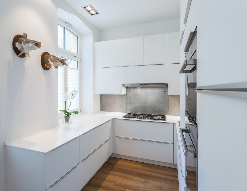 Inspiration for a small contemporary u-shaped separate kitchen in Cologne with flat-panel cabinets, white cabinets, stainless steel appliances, medium hardwood floors, no island, grey splashback and glass sheet splashback.