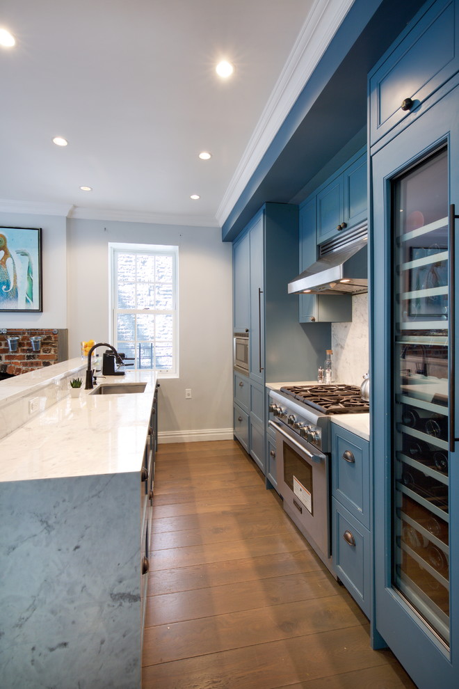 This is an example of a mid-sized eclectic kitchen in New York with recessed-panel cabinets, blue cabinets, marble benchtops, grey splashback, marble splashback, stainless steel appliances, medium hardwood floors, a peninsula and brown floor.