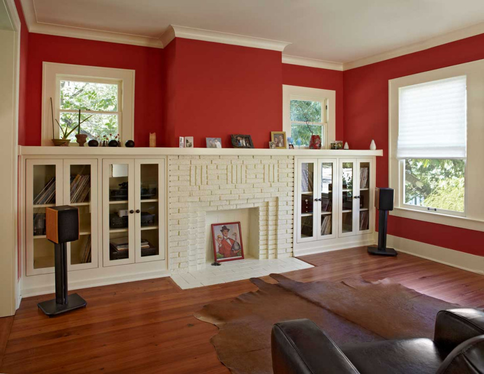 На фото: изолированная гостиная комната среднего размера в стиле кантри с красными стенами, паркетным полом среднего тона, стандартным камином, фасадом камина из кирпича, коричневым полом, деревянными стенами и акцентной стеной с