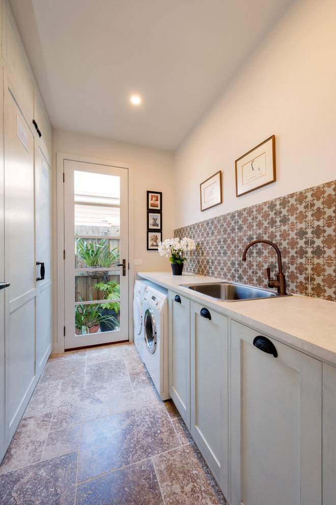This is an example of a small mediterranean galley dedicated laundry room in Melbourne with a drop-in sink, shaker cabinets, white cabinets, white walls, travertine floors, a side-by-side washer and dryer and laminate benchtops.