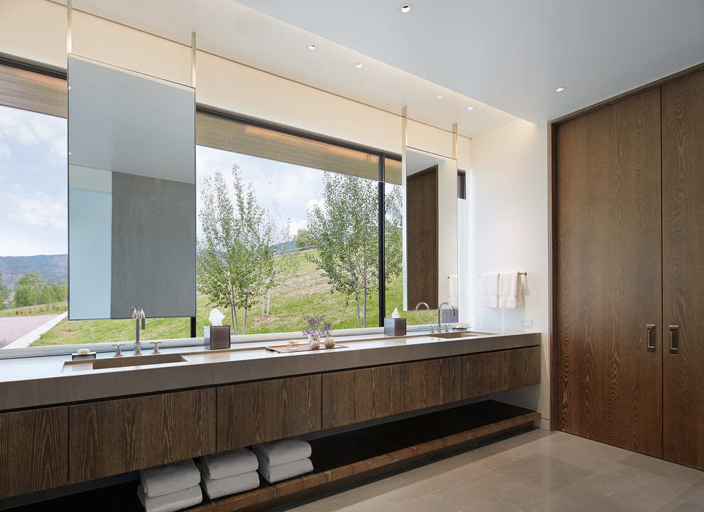 Photo of a contemporary bathroom in Denver with flat-panel cabinets, white tile, white walls, limestone floors, an integrated sink, limestone benchtops, grey floor, dark wood cabinets and grey benchtops.