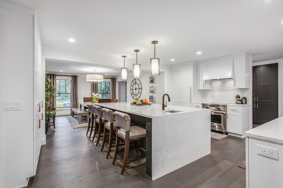 Large contemporary galley kitchen in Grand Rapids with a farmhouse sink, shaker cabinets, white cabinets, quartz benchtops, stainless steel appliances, medium hardwood floors, with island and brown floor.