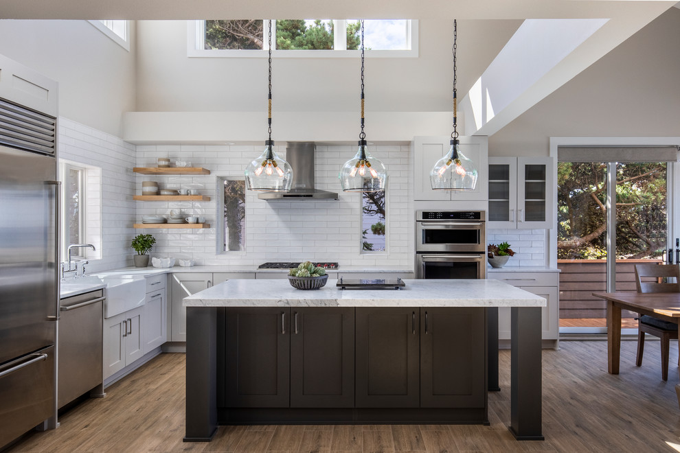 Inspiration for a mid-sized beach style l-shaped eat-in kitchen in Portland with a farmhouse sink, shaker cabinets, grey cabinets, marble benchtops, white splashback, subway tile splashback, stainless steel appliances, porcelain floors, with island, brown floor and white benchtop.