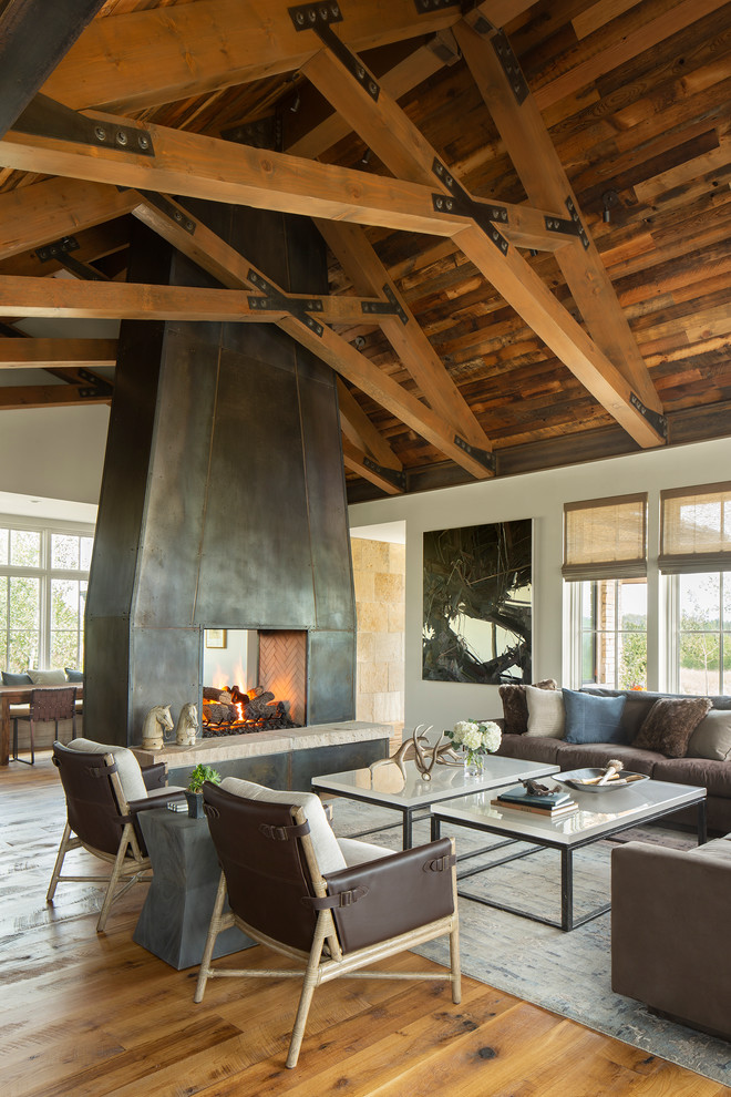 Inspiration for a country open concept living room in Denver with white walls, medium hardwood floors, a two-sided fireplace, a metal fireplace surround and brown floor.