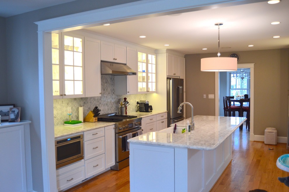Inspiration for a mid-sized arts and crafts galley open plan kitchen in DC Metro with a farmhouse sink, shaker cabinets, white cabinets, granite benchtops, grey splashback, ceramic splashback, stainless steel appliances, light hardwood floors and with island.