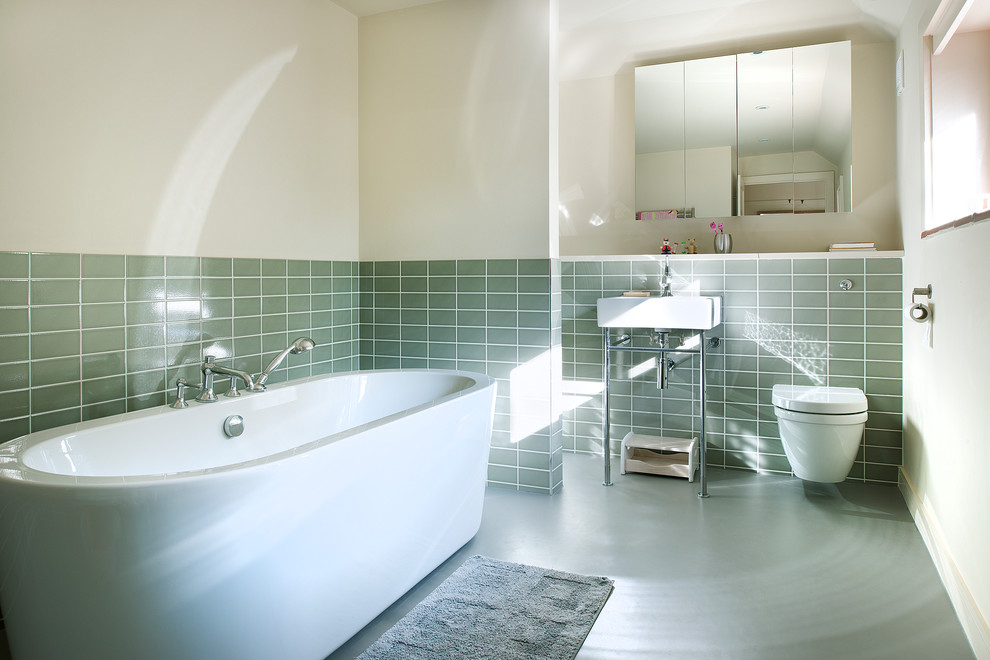 Photo of a mid-sized contemporary bathroom in Hampshire with a freestanding tub, a wall-mount toilet, ceramic tile, white walls, linoleum floors, green tile and a console sink.