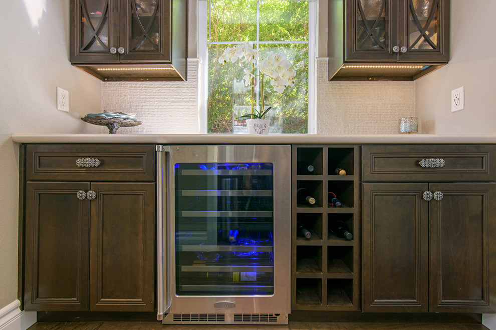 Open concept kitchen - large transitional l-shaped medium tone wood floor and brown floor open concept kitchen idea in San Diego with recessed-panel cabinets, dark wood cabinets, quartz countertops, beige backsplash, travertine backsplash, paneled appliances and an island