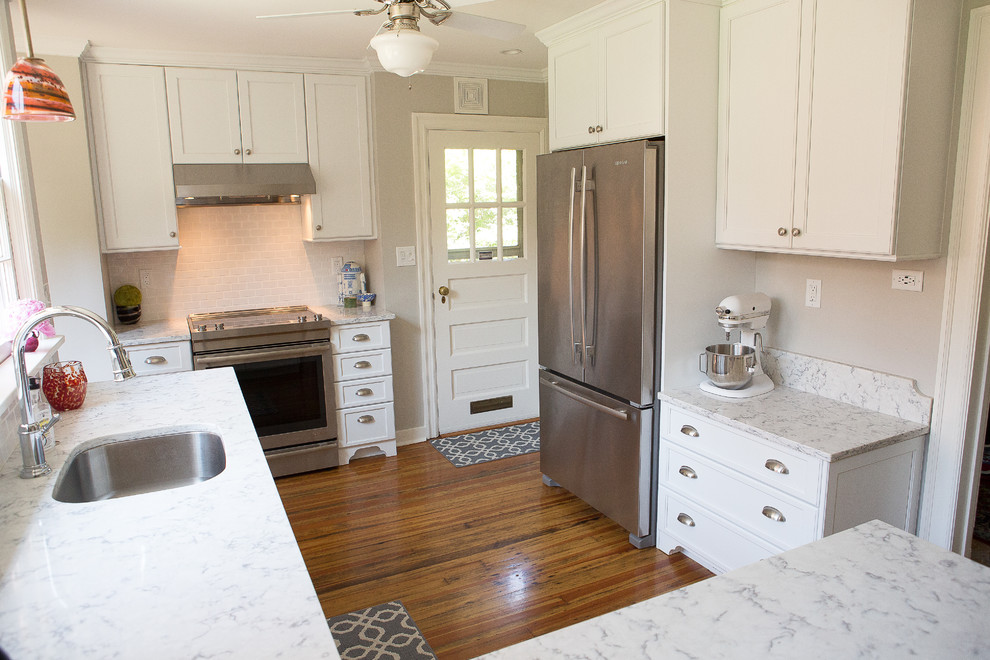 Example of a small transitional light wood floor kitchen design with an undermount sink, shaker cabinets, white cabinets, quartz countertops, white backsplash, porcelain backsplash, stainless steel appliances and a peninsula