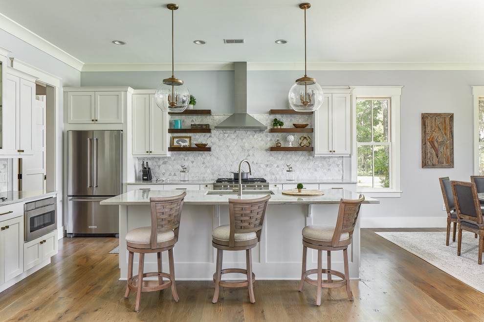 This is an example of a large beach style u-shaped eat-in kitchen in Charleston with an undermount sink, shaker cabinets, white cabinets, grey splashback, stainless steel appliances, light hardwood floors, with island, grey benchtop and quartzite benchtops.