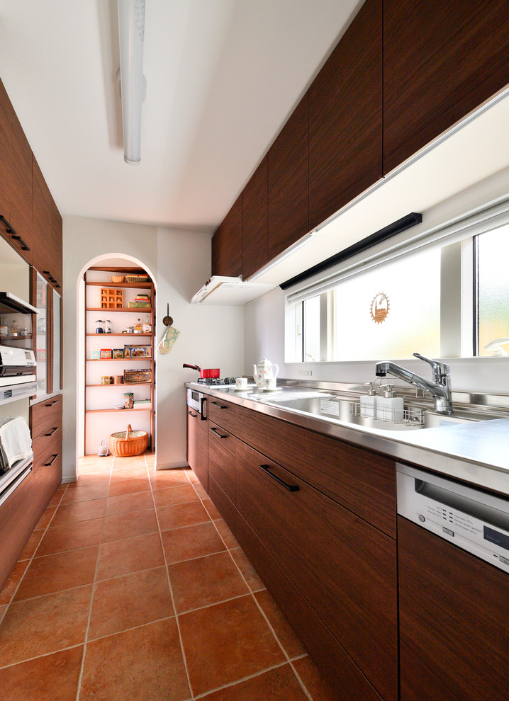 Photo of a contemporary single-wall separate kitchen in Other with a single-bowl sink, flat-panel cabinets, medium wood cabinets, stainless steel benchtops, white splashback, terra-cotta floors, a peninsula and brown floor.