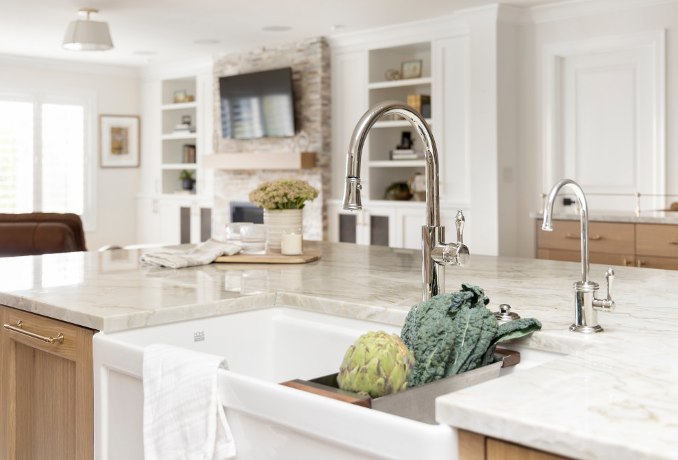 This is an example of a large beach style l-shaped open plan kitchen in Portland with a farmhouse sink, recessed-panel cabinets, white cabinets, quartzite benchtops, white splashback, ceramic splashback, stainless steel appliances, medium hardwood floors, with island and beige benchtop.