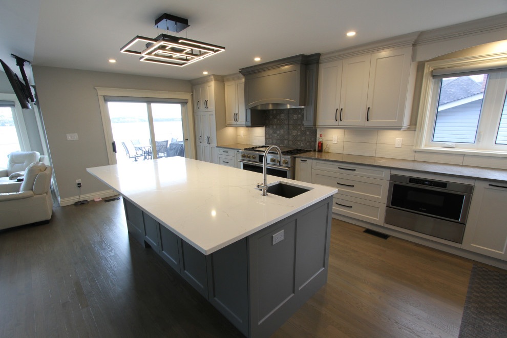 Exempel på ett stort modernt vit vitt kök, med en undermonterad diskho, luckor med infälld panel, vita skåp, bänkskiva i kvarts, vitt stänkskydd, stänkskydd i porslinskakel, rostfria vitvaror, laminatgolv, en köksö och grått golv
