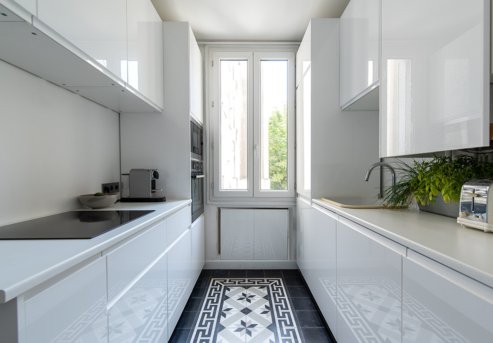 This is an example of a small contemporary galley separate kitchen in Paris with a drop-in sink, flat-panel cabinets, white cabinets, white splashback, black floor, white benchtop, stainless steel appliances, cement tiles and no island.