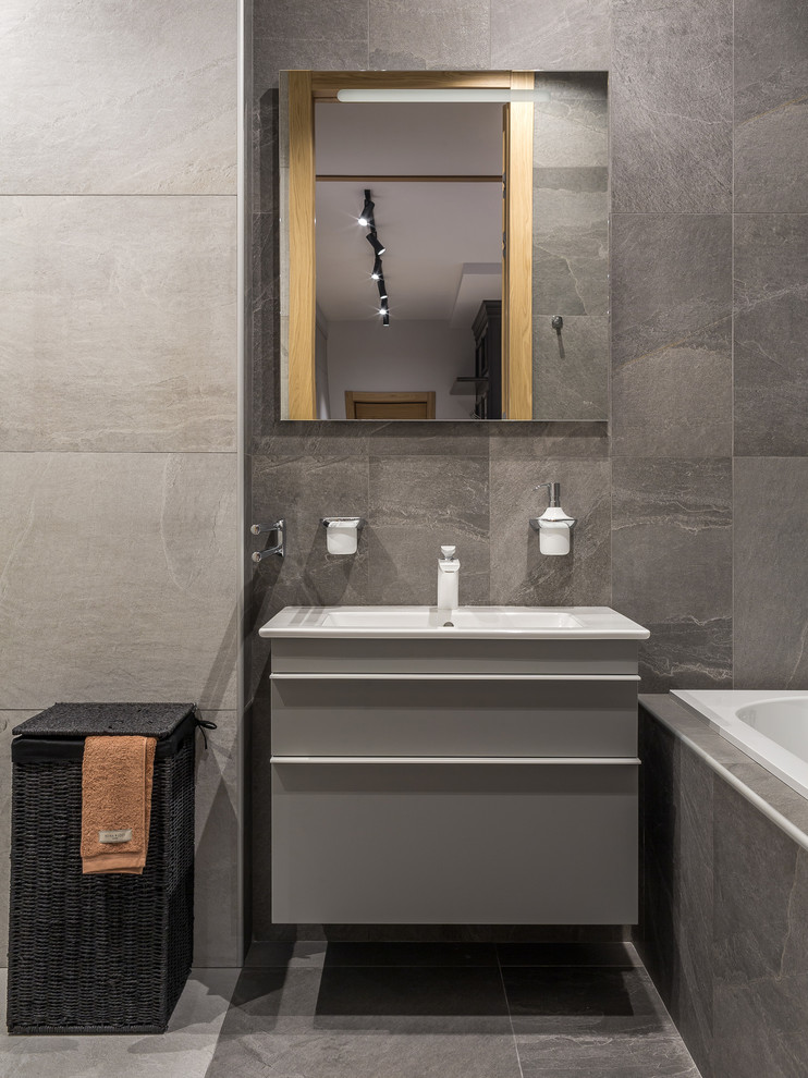 Inspiration for a mid-sized contemporary master bathroom in Other with flat-panel cabinets, grey cabinets, an undermount tub, a shower/bathtub combo, a wall-mount toilet, gray tile, porcelain tile, grey walls, porcelain floors, a wall-mount sink, grey floor and an open shower.
