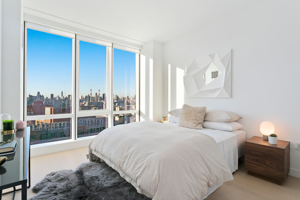This is an example of a contemporary guest bedroom in New York with white walls, light hardwood floors and beige floor.