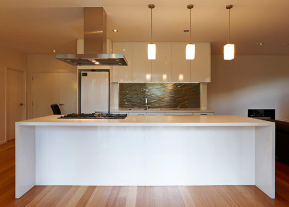 Inspiration for a large contemporary galley eat-in kitchen in Melbourne with an undermount sink, flat-panel cabinets, white cabinets, quartz benchtops, grey splashback, glass sheet splashback, white appliances, medium hardwood floors and with island.
