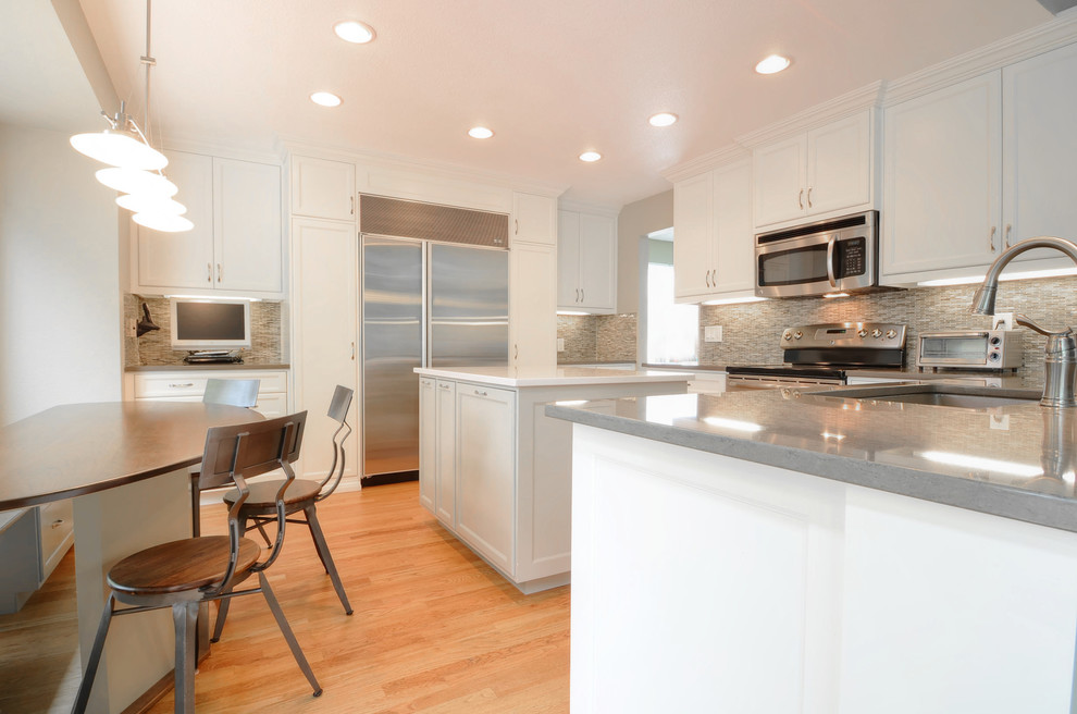 Mid-sized traditional u-shaped eat-in kitchen in Denver with an undermount sink, recessed-panel cabinets, white cabinets, granite benchtops, beige splashback, stone tile splashback, stainless steel appliances, medium hardwood floors and with island.