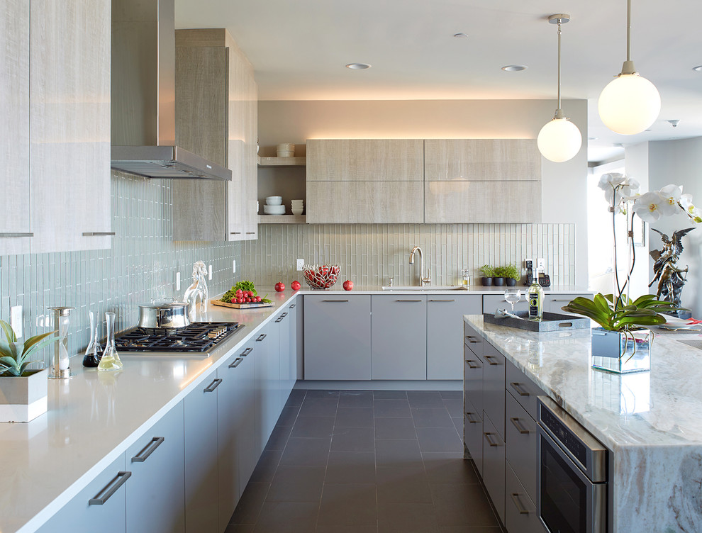 Photo of an expansive contemporary l-shaped kitchen in New York with an undermount sink, flat-panel cabinets, grey cabinets, quartz benchtops, grey splashback, glass tile splashback, stainless steel appliances, porcelain floors, with island, grey floor and white benchtop.