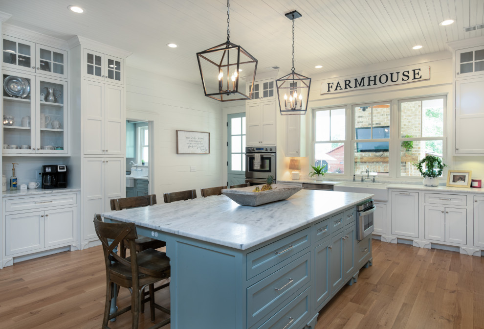 Photo of a large country l-shaped eat-in kitchen in Other with a farmhouse sink, flat-panel cabinets, white cabinets, granite benchtops, brown splashback, brick splashback, stainless steel appliances, light hardwood floors, with island, beige floor and white benchtop.