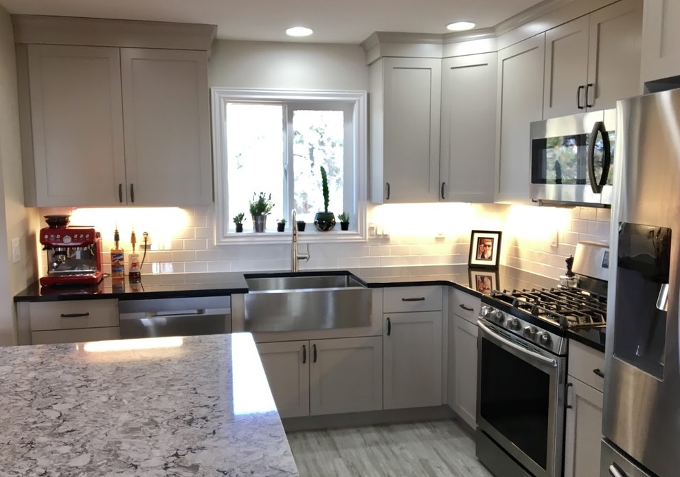 Photo of a mid-sized country l-shaped separate kitchen in Denver with a farmhouse sink, shaker cabinets, beige cabinets, quartz benchtops, white splashback, stainless steel appliances, vinyl floors, with island, subway tile splashback and grey floor.