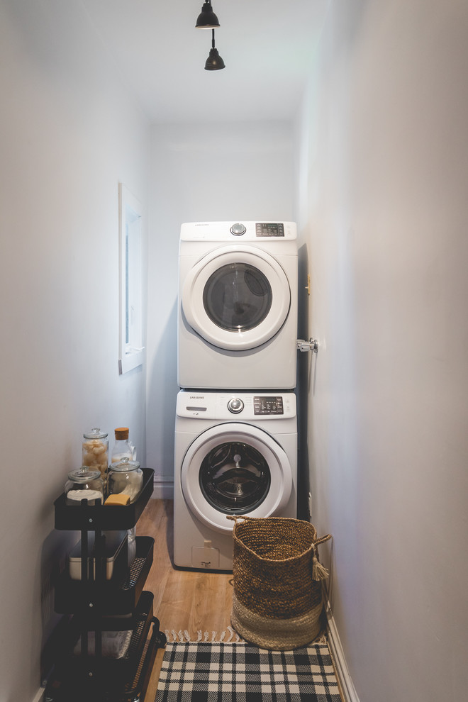 This is an example of a mid-sized scandinavian galley dedicated laundry room in Montreal with flat-panel cabinets, white cabinets, white walls and a side-by-side washer and dryer.