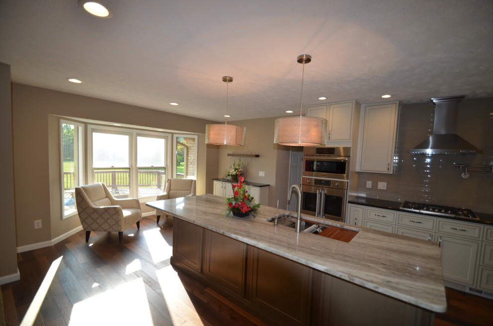 Example of a mid-sized transitional u-shaped medium tone wood floor and brown floor eat-in kitchen design with an undermount sink, raised-panel cabinets, beige cabinets, granite countertops, multicolored backsplash, mosaic tile backsplash, stainless steel appliances, an island and multicolored countertops
