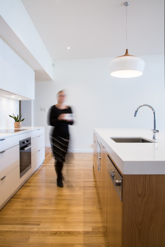 This is an example of a mid-sized contemporary open plan kitchen in Adelaide with an undermount sink, white cabinets, quartz benchtops, white splashback, stone slab splashback, stainless steel appliances, medium hardwood floors and with island.
