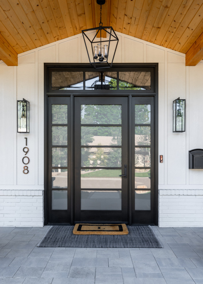 Example of a cottage concrete floor, gray floor, vaulted ceiling and shiplap wall single front door design in Denver with white walls and a black front door