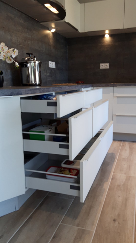 This is an example of a mid-sized contemporary l-shaped eat-in kitchen in Marseille with an undermount sink, beaded inset cabinets, white cabinets, laminate benchtops, grey splashback, stainless steel appliances, ceramic floors and with island.