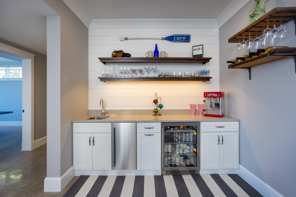 This is an example of a mid-sized traditional single-wall wet bar in Other with an undermount sink, shaker cabinets, white cabinets, white splashback, shiplap splashback, concrete floors and beige floor.