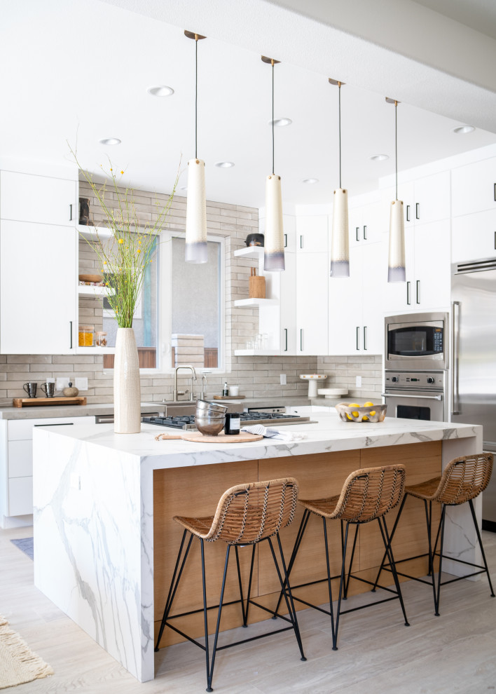 Contemporary u-shaped kitchen in Orange County with a farmhouse sink, flat-panel cabinets, white cabinets, white splashback, stainless steel appliances, light hardwood floors, beige floor and multi-coloured benchtop.