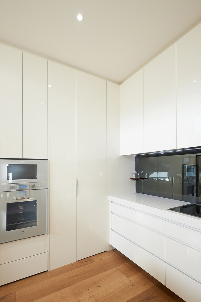 Inspiration for a mid-sized contemporary l-shaped eat-in kitchen in Melbourne with flat-panel cabinets, white cabinets, metallic splashback, stainless steel appliances, medium hardwood floors, a double-bowl sink, marble benchtops, mirror splashback and a peninsula.