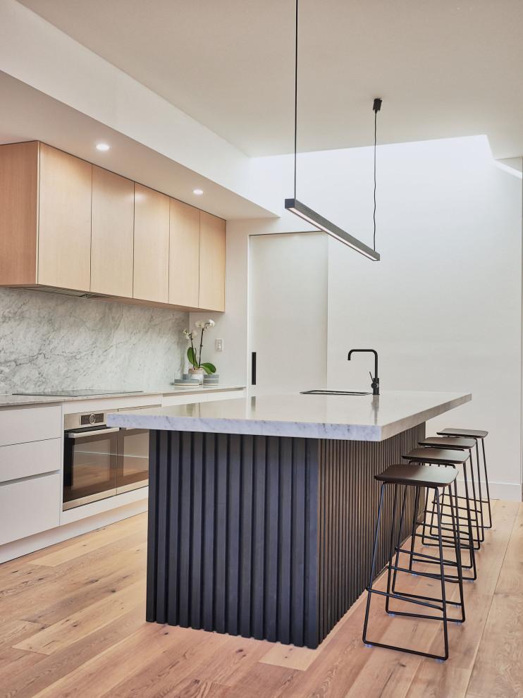 Mid-sized scandinavian galley open plan kitchen in Melbourne with a drop-in sink, grey splashback, stainless steel appliances, light hardwood floors and with island.