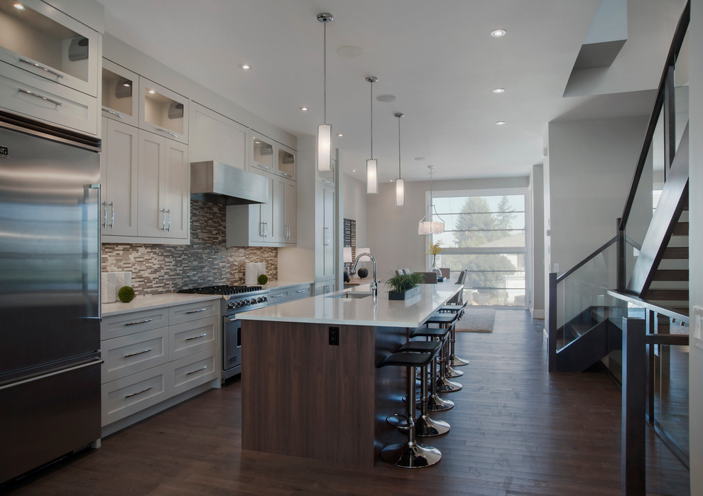 This is an example of a large contemporary u-shaped open plan kitchen in Calgary with an undermount sink, shaker cabinets, white cabinets, quartz benchtops, multi-coloured splashback, matchstick tile splashback, stainless steel appliances, dark hardwood floors and with island.
