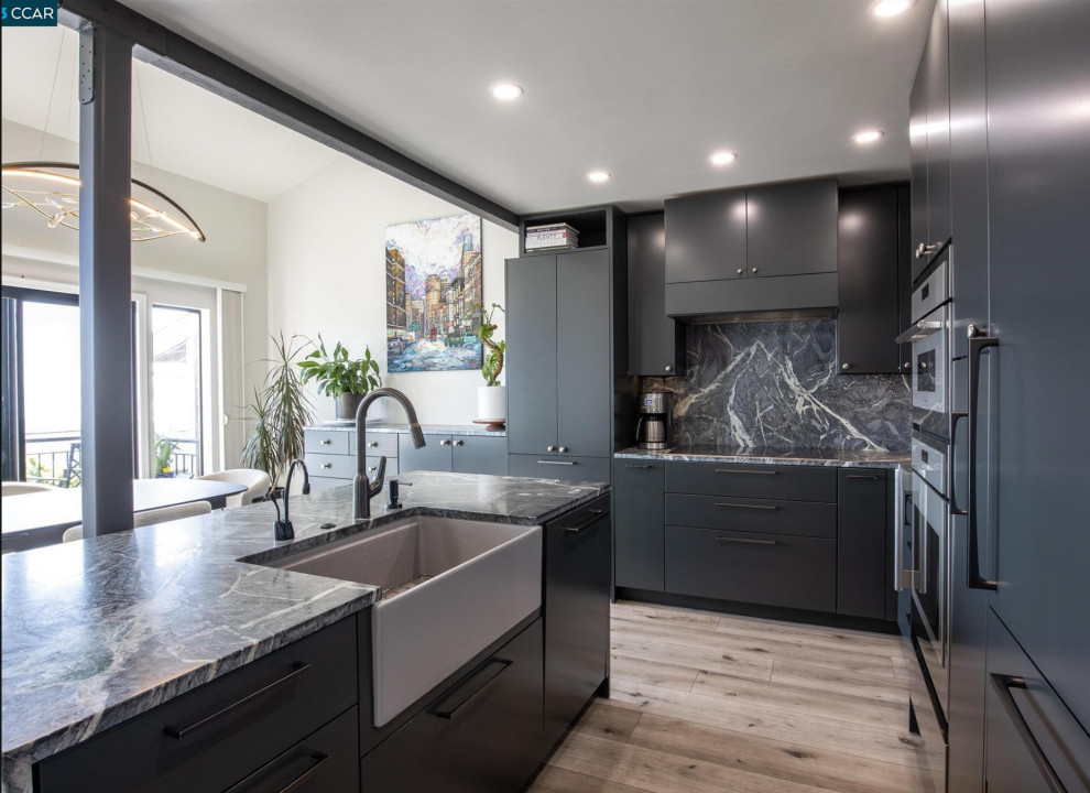 This is an example of a small contemporary l-shaped eat-in kitchen in San Francisco with a farmhouse sink, flat-panel cabinets, black cabinets, soapstone benchtops, multi-coloured splashback, black appliances, vinyl floors, with island, brown floor, multi-coloured benchtop and vaulted.