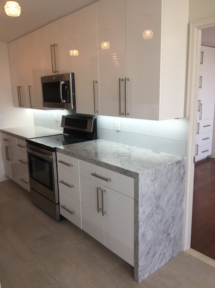 This is an example of a mid-sized modern galley separate kitchen in New York with porcelain floors, beige floor, a farmhouse sink, stainless steel appliances, flat-panel cabinets, white cabinets, quartzite benchtops, grey splashback, glass tile splashback and no island.