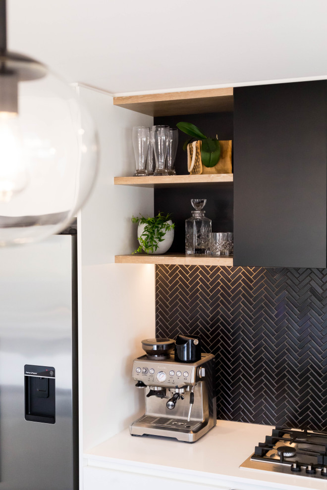 Photo of a mid-sized scandinavian galley eat-in kitchen in Auckland with a double-bowl sink, flat-panel cabinets, black cabinets, solid surface benchtops, black splashback, mosaic tile splashback, stainless steel appliances, porcelain floors, with island, grey floor and white benchtop.