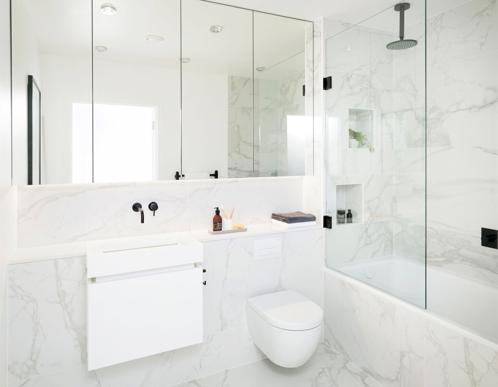 This is an example of a mid-sized contemporary bathroom in London with flat-panel cabinets, white cabinets, a drop-in tub, a wall-mount toilet, porcelain tile, porcelain floors, a wall-mount sink, granite benchtops, an alcove shower, gray tile, white tile, multi-coloured walls, an open shower and a niche.