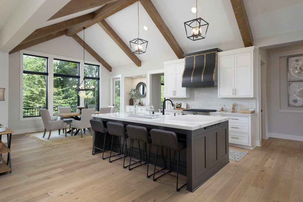 Transitional galley kitchen in Minneapolis with a farmhouse sink, shaker cabinets, white cabinets, white splashback, stainless steel appliances, light hardwood floors, with island, beige floor, white benchtop, exposed beam and vaulted.