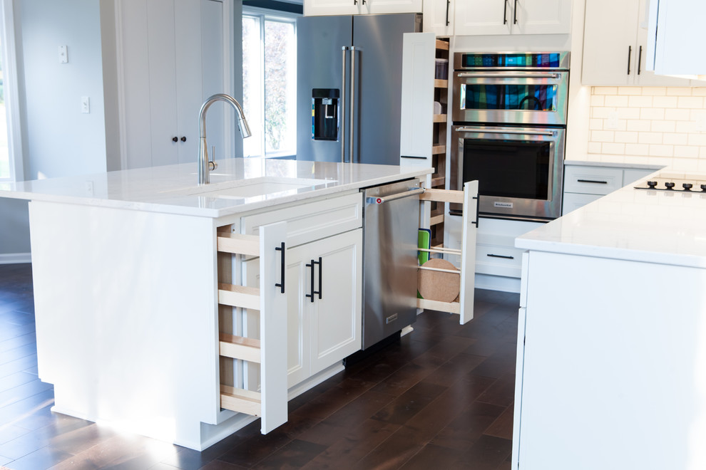 Large transitional l-shaped dark wood floor and brown floor eat-in kitchen photo with an undermount sink, recessed-panel cabinets, white cabinets, quartz countertops, white backsplash, subway tile backsplash, stainless steel appliances and an island