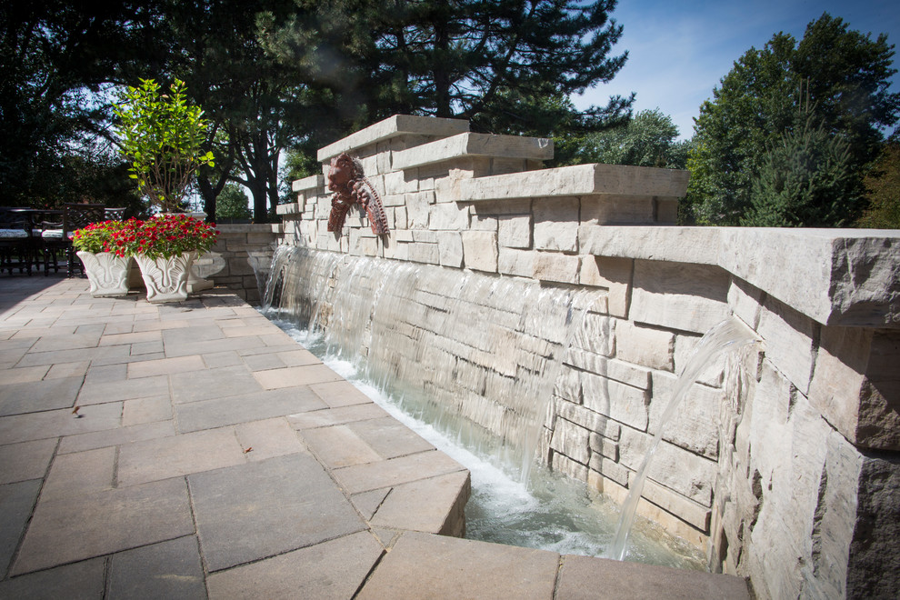 This is an example of a transitional backyard stone water fountain landscape in Omaha.