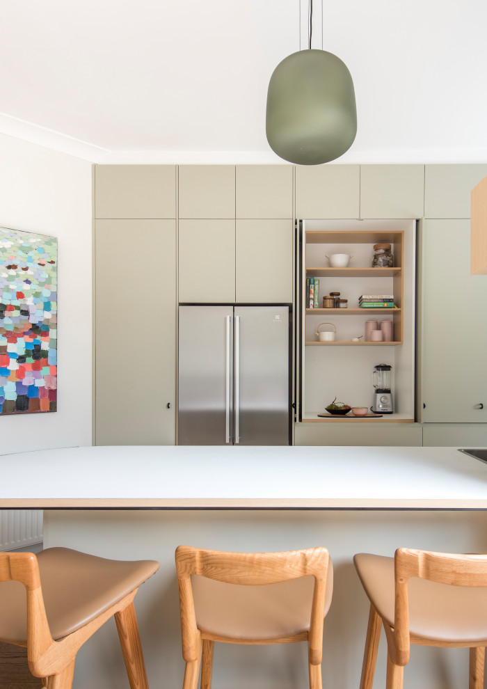 Contemporary u-shaped eat-in kitchen in Melbourne with a double-bowl sink, flat-panel cabinets, beige cabinets, solid surface benchtops, beige splashback, ceramic splashback, stainless steel appliances, medium hardwood floors, with island, brown floor and white benchtop.