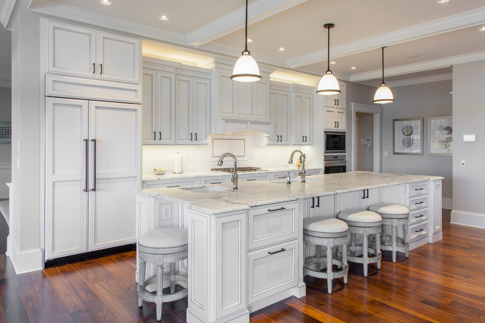 Design ideas for a large arts and crafts galley open plan kitchen in Burlington with a farmhouse sink, recessed-panel cabinets, white cabinets, marble benchtops, white splashback, stone tile splashback, panelled appliances, dark hardwood floors and with island.