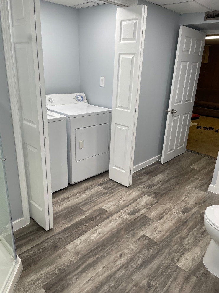 Photo of a large contemporary bathroom in Other with white cabinets, a corner shower, a one-piece toilet, grey walls, vinyl flooring, an integrated sink, grey floors, a hinged door, white worktops, a laundry area, a single sink and a freestanding vanity unit.