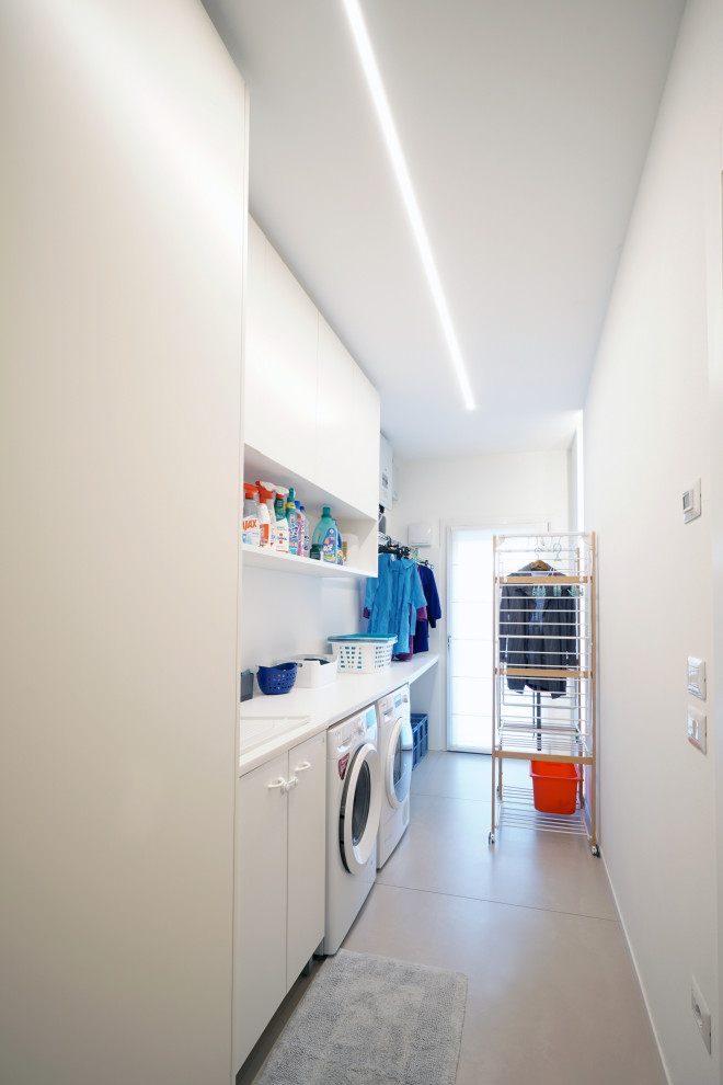 Inspiration for a small contemporary single-wall utility room in Venice with a drop-in sink, flat-panel cabinets, white cabinets, solid surface benchtops, white splashback, porcelain splashback, white walls, porcelain floors, a side-by-side washer and dryer, beige floor and white benchtop.